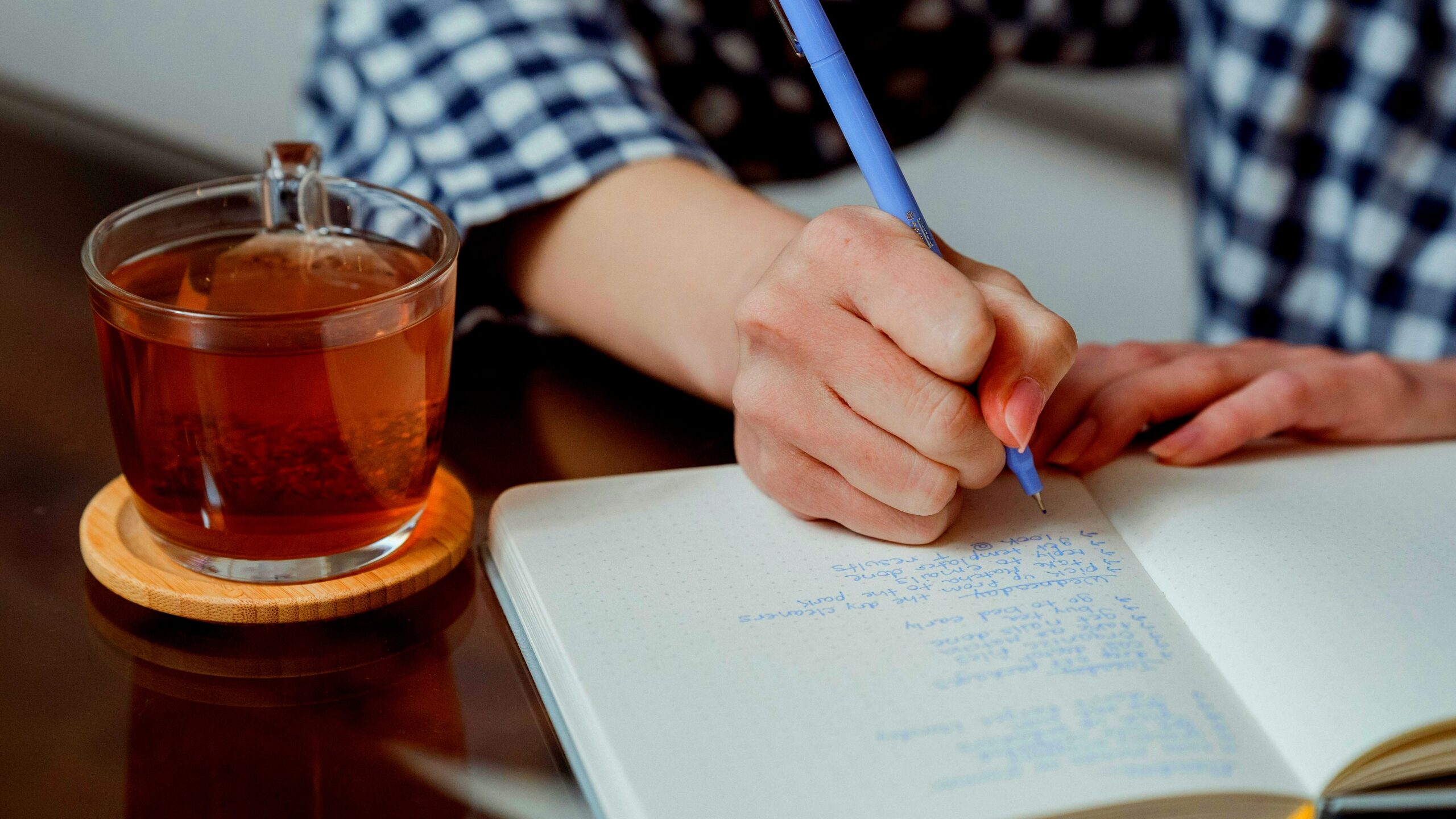 Person writing in a journal with a cup of coffee, representing personal growth habits like daily reflection and goal setting